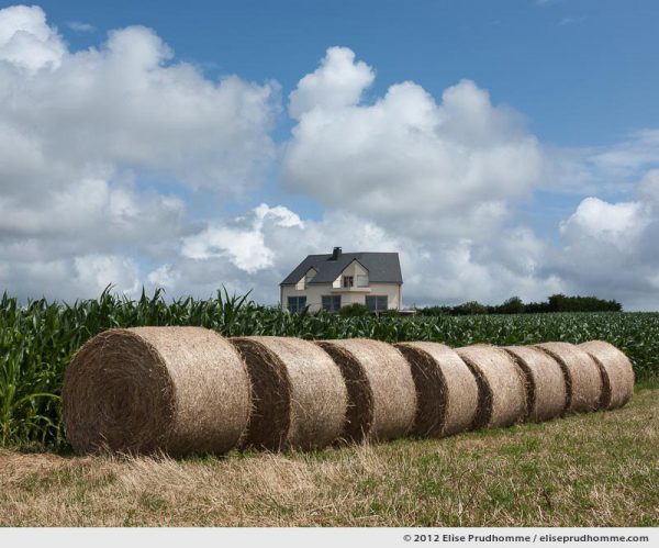 Prefab house and hay bales under a cloudy sky, Normandy, France, 2012 by Elise Prudhomme