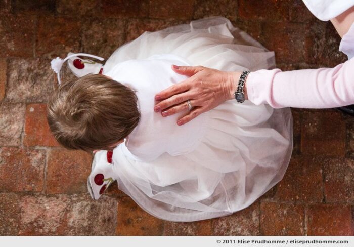 A loving grandmother caresses the back of a baby girl in a pink christening gown, Angers, France, 2011 by Elise Prudhomme