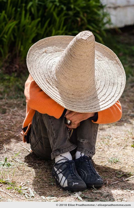 Boy sitting in a garden hidden under a sombrero, Normandy, France, 2010 by Elise Prudhomme.