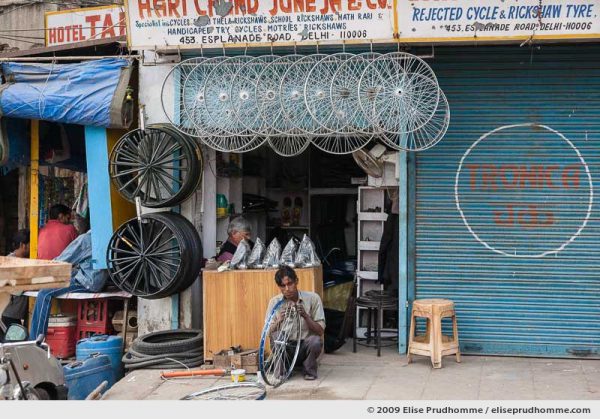Man repairing a bicycle wheel in front of a repair shop on Esplanade Road, Delhi, India, 2009 by Elise Prudhomme.