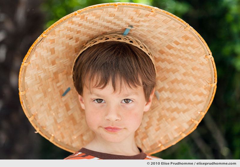Portrait of a brown-eyed boy wearing a bamboo rain hat, Normandy, France, 2010 by Elise Prudhomme.