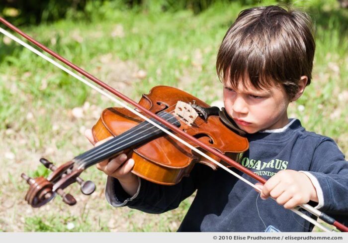 Serious boy playing the violin outside in a garden, Normandy, France, 2010 by Elise Prudhomme.