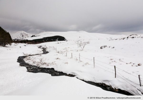 Snow covered hills and stream running through, Banne d'Ordanche, Auvergne, France, 2010 by Elise Prudhomme.