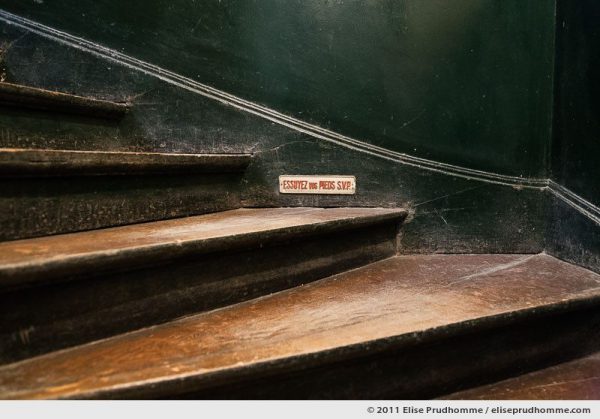 Wipe Your Feet Please sign in an old fashioned Parisian staircase, France, 2011 by Elise Prudhomme.