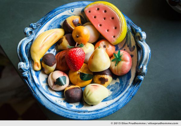 Choice of fruit shaped marzipan sweets, influenced by Silician culinary traditions, displayed in a traditional blue ceramic bowl made in Cefalu, Sicily. Frutta Martorana, fruit de marzipan sicilien fait main traditionnel dans un bol en ceramique bleu de Cefalu, Sicile.