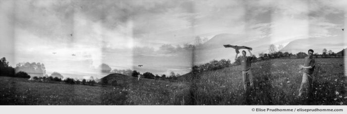 Black and white panoramic photograph of a young man flying a Chinese kite in Saint Ours, France. Analog photography series entitled Lieux-dits by Elise Prudhomme.