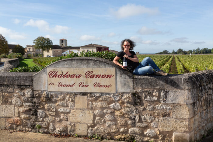Elise Prudhomme posing with a bottle of Three Feathers Estate Pinot Noir in front of the vineyards at Chateau Canon 1er Grand Cru Classe, Saint Emilion in the Bordeaux wine region of France.