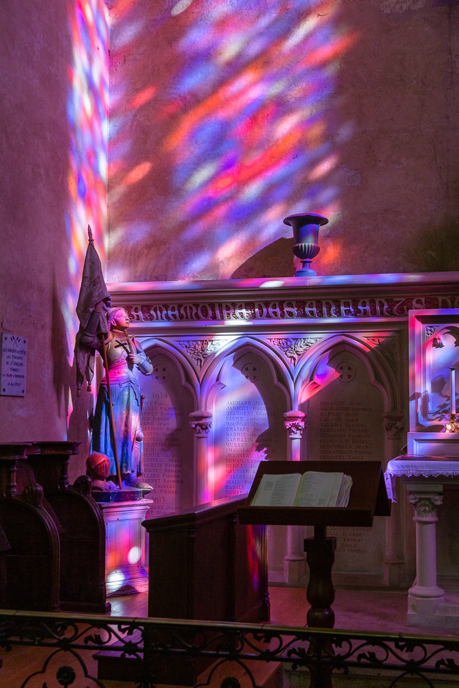 Daylight shining through stained glass onto the Joan of Arc statue in the Collegiale Church of Saint-Emilion, Gironde, France.